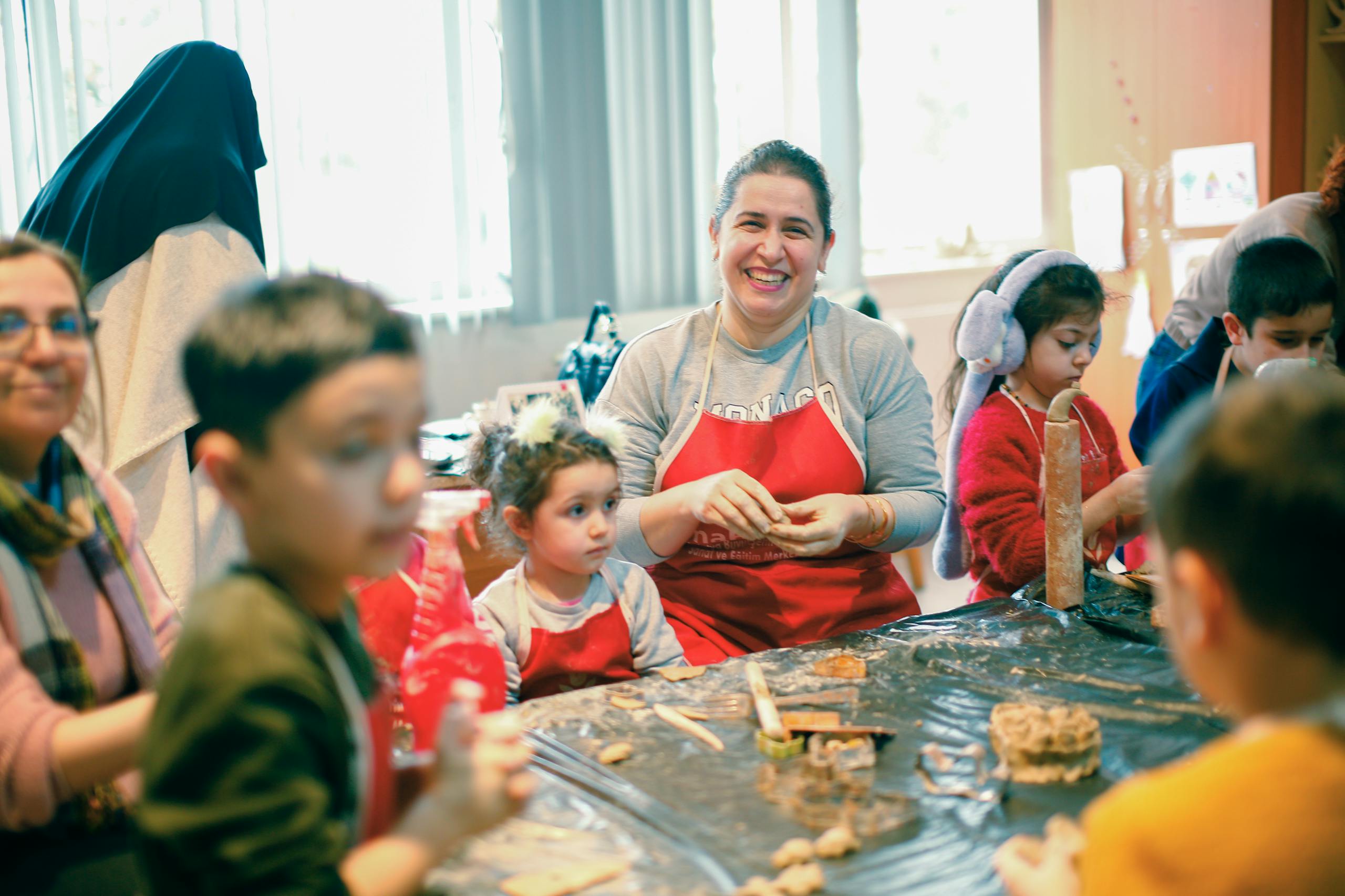 A woman in an apron and red shirt is teaching children how to make cookies